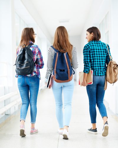 Cute students with rucksacks walking down college corridor